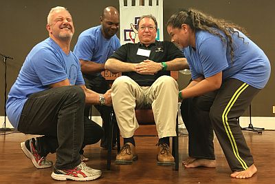 Tom Hudspeth sits in a chair, three other people lift him.