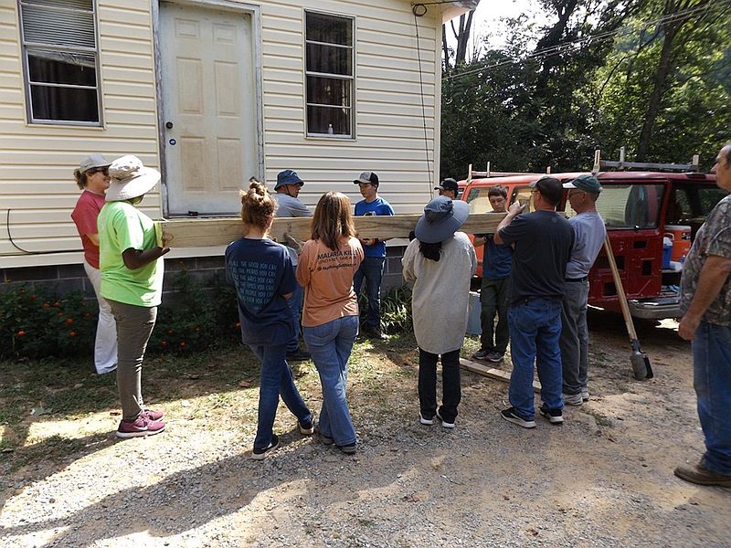 a group lifts a large board, behind is a door above ground level