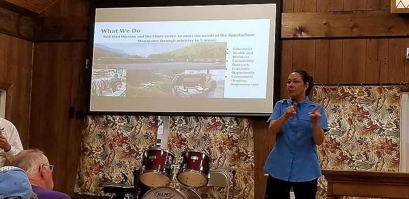 a woman speaks and signs with a projected picture about the mission behind her