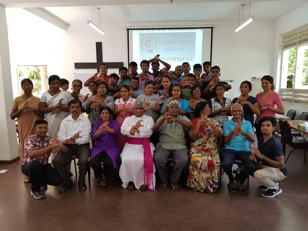 people in a classroom, using sign language, in the back is a display for Methodist Church Sri Lanka, Deaf Conference